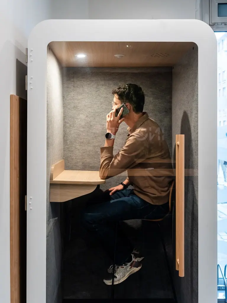 Homme assis dans une cabine insonorisée, téléphonant dans un espace de travail moderne et fonctionnel