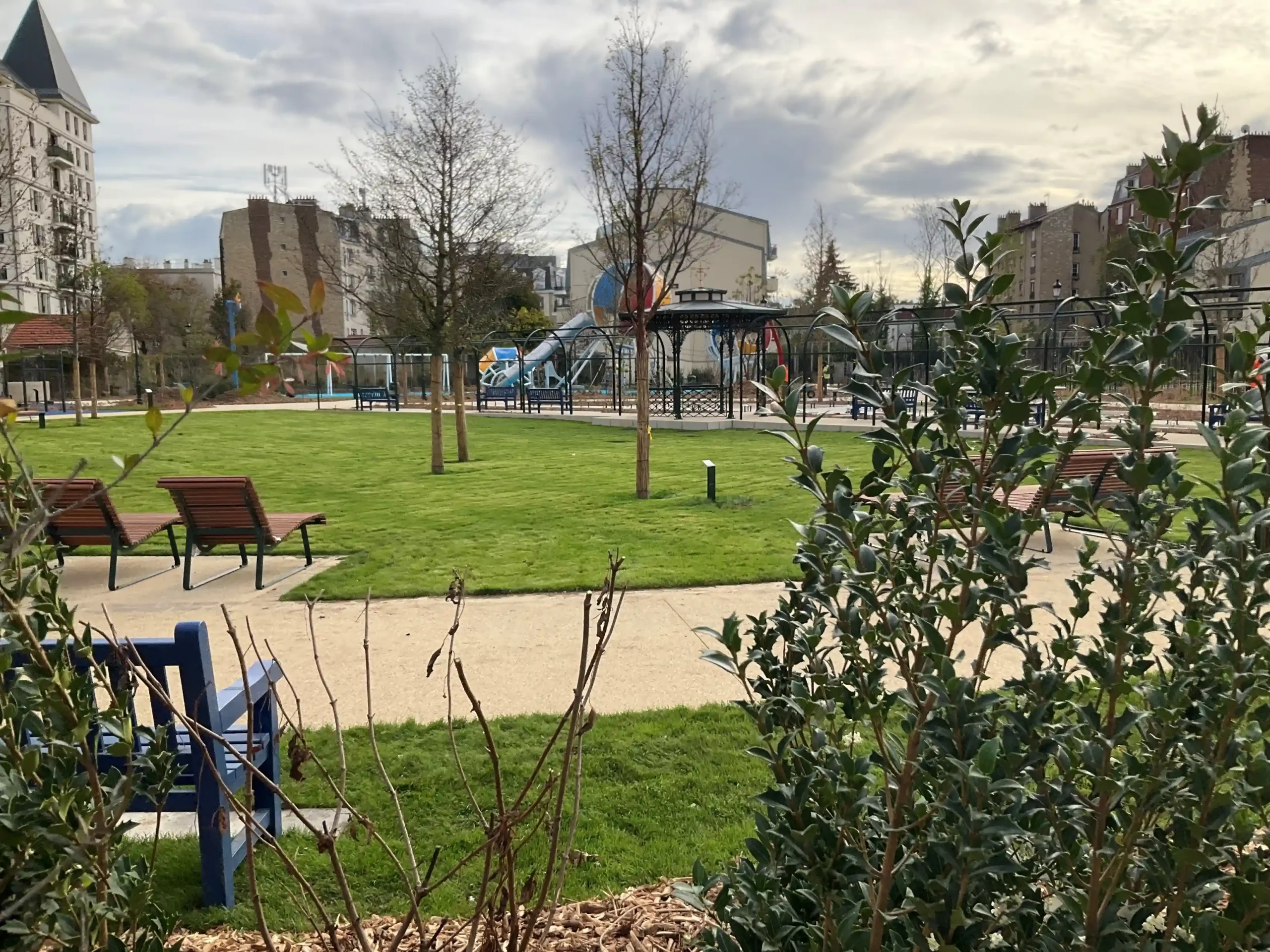 Espace vert aménagé avec pelouse, bancs et aire de jeux à Puteaux, sous un ciel nuageux.